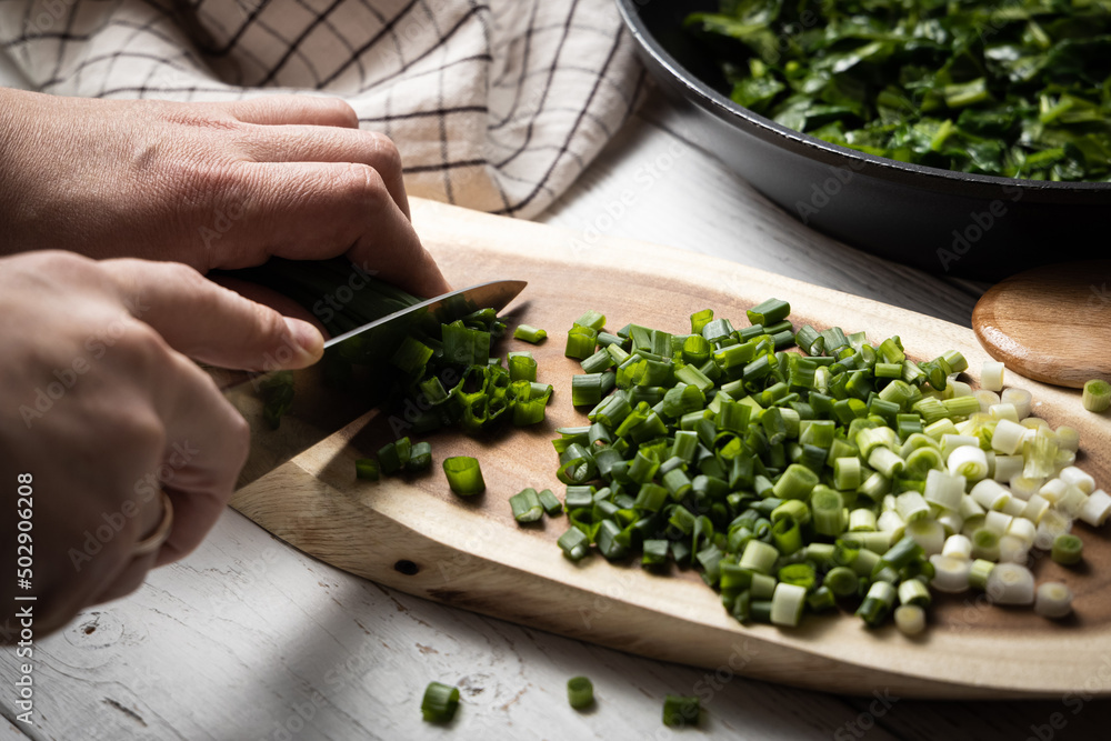A man with a knife on a wooden board cuts green onions. A man with a knife on a wooden board cuts green onions.