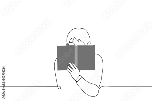 man sitting hiding his face behind an open book - one line drawing vector. concept of reading a shameful book, forbidden literature, guilty pleasure, erotic novel