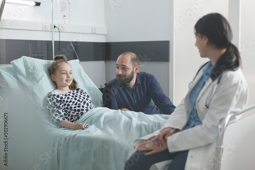 Pediatric clinic medic specialist explaining to stressed uneasy man illness symptoms and viable treatment for daughter. Ill little child resting in pediatric clinic bed in recovery ward room.