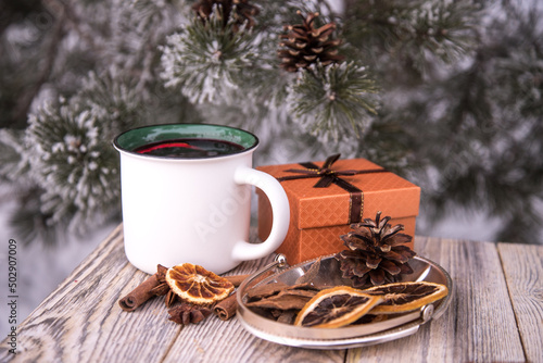Ceramic white mug with mulled wine gift box and spices on a wooden table in winter.