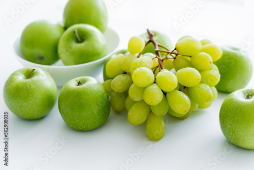 green and ripe apples in bowl near grapes on white.