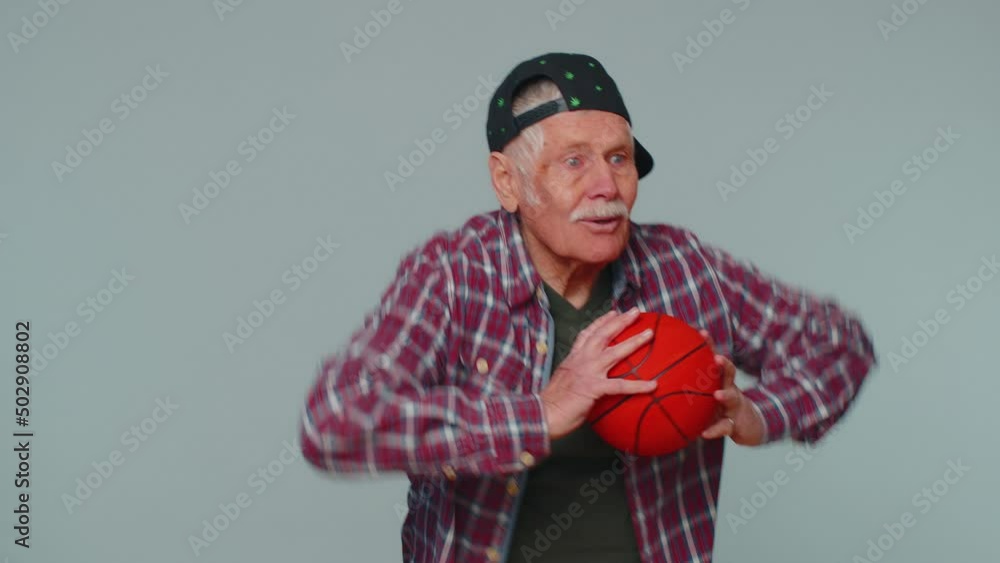 Senior man sportsman basketball fan holding ball looking at camera, training dribbling. Workout sport motivation lifestyle concept. Elderly grandfather isolated alone on gray studio wall background Senior man sportsman basketball fan holding ball looking at camera, training dribbling. Workout sport motivation lifestyle concept. Elderly grandfather isolated alone on gray studio wall background