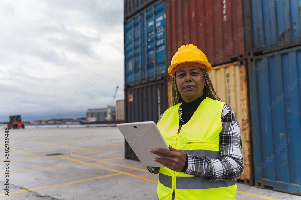 Woman in a reflective waistcoat and hard hat looking at the camera while using a tablet on the dock