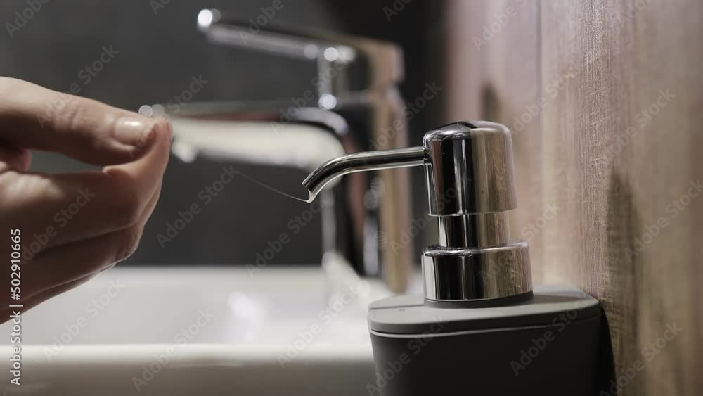 Woman pushes the dispenser and the liquid soap is squeezed in her hand. Woman washing her hands in the bathroom using a mild gel for advanced skin care and disinfection. Woman pushes the dispenser and the liquid soap is squeezed in her hand. Woman washing her hands in the bathroom using a mild gel for advanced skin care and disinfection.