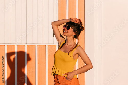 Young woman in tank top and orange standing still near orange beach house. #502915699