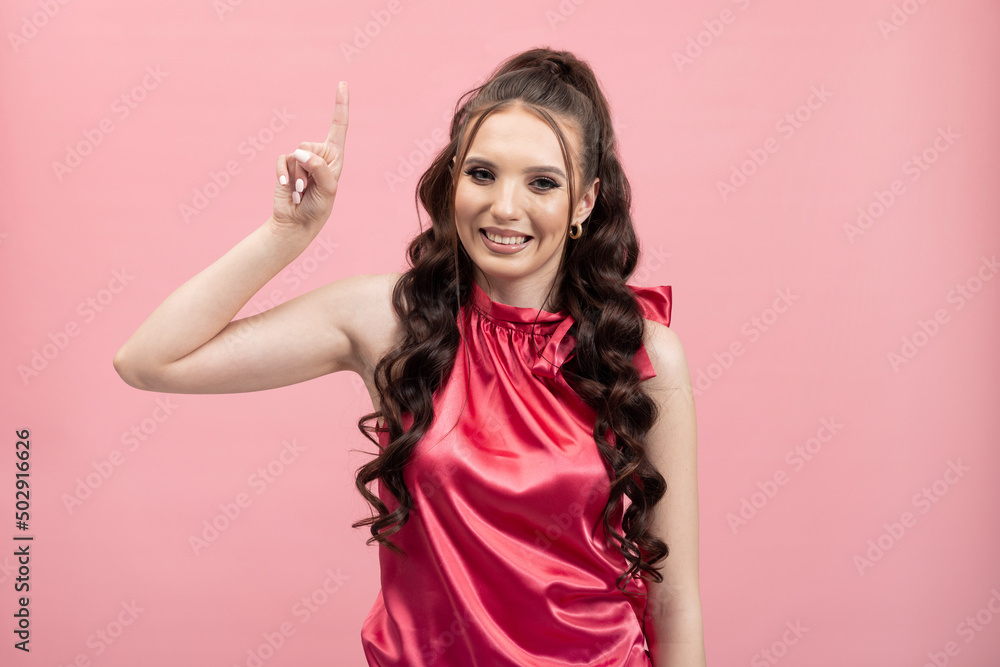 Photo of excited, smiling young woman dressed in businesswoman jacket pointing finger at empty space, isolated, pink background. Photo of excited, smiling young woman dressed in businesswoman jacket pointing finger at empty space, isolated, pink background.