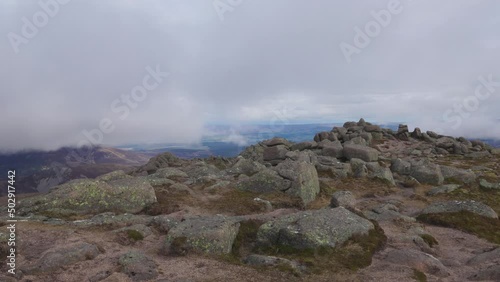 A 360° footage of a Scottish mountain summit (Bynack More) with a cairn and surrounding mountain summits under a cloudy sky and stormy weather