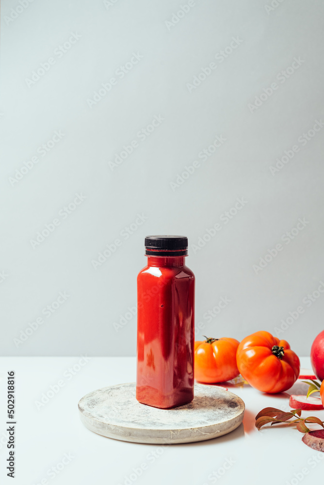 Red smoothie drink in bottle surrounded by red apples, tomatoes and beets, front view Red smoothie drink in bottle surrounded by red apples, tomatoes and beets, front view