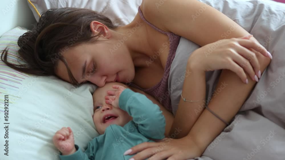 young mother and her infant baby having fun playing in bed morning. mom and baby child together spending time cuddling in bedroom waking up. young mother and her infant baby having fun playing in bed morning. mom and baby child together spending time cuddling in bedroom waking up.