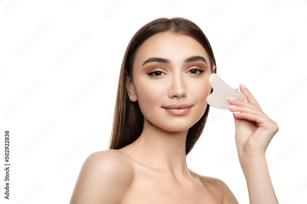 Portrait of beautiful young girl using face cosmetology tool for massage isolated over white background. Face contouring