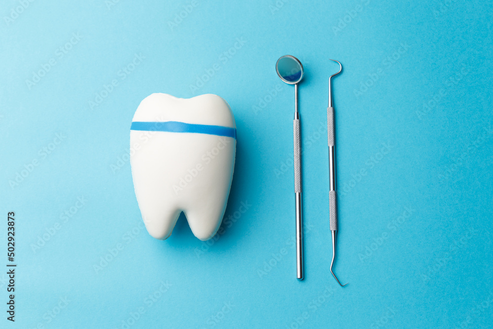 The concept of oral health. Tooth, diagnostic bilateral periodontal probe and diagnostic dental mirror made of stainless steel. Dental equipment is highlighted on a blue background in close-up. The concept of oral health. Tooth, diagnostic bilateral periodontal probe and diagnostic dental mirror made of stainless steel. Dental equipment is highlighted on a blue background in close-up.