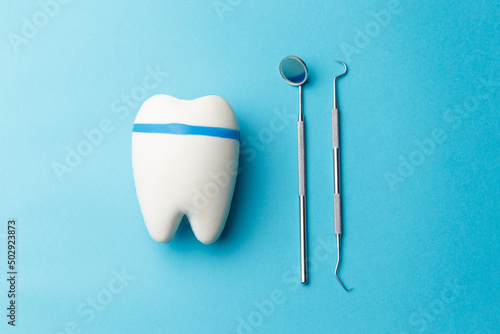 The concept of oral health. Tooth, diagnostic bilateral periodontal probe and diagnostic dental mirror made of stainless steel. Dental equipment is highlighted on a blue background in close-up. © Evgenii