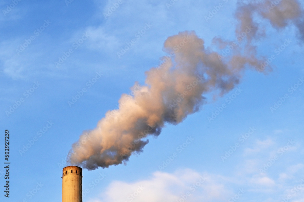 Smoke billowing out the tall chimeny of a power station at dusk isolated against a blue sky. No people. Copy space. Smoke billowing out the tall chimeny of a power station at dusk isolated against a blue sky. No people. Copy space.