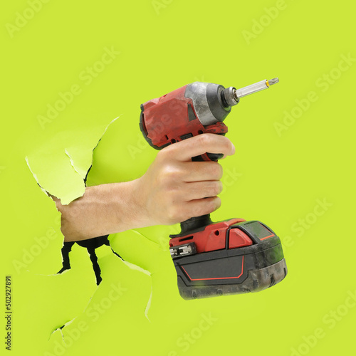 Man hand holds brushless cordless impact driver that breaks through bright green wall