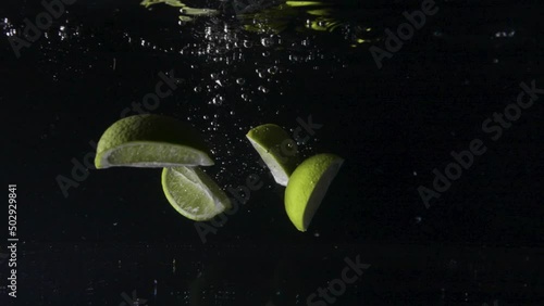 Slow motion underwater shot of fresh juicy green limes falling into the water and spreading out, then floating back up, close up, cut out photo