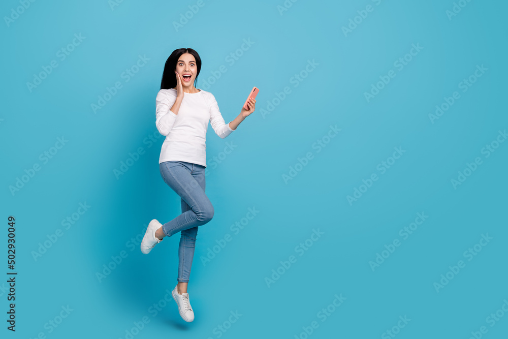 Full length body size view of beautiful trendy amazed girly girl jumping using gadget app isolated on bright blue color background