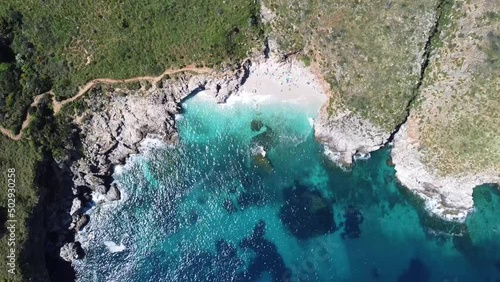 imposing green cliffs over a perfect little bay with white sand, near zingaro in sicily in italy, nice weather (droneshot) photo