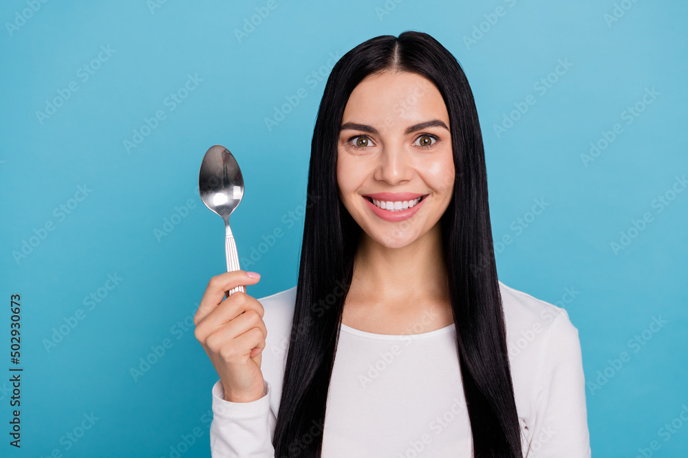 Photo of young cute brunette lady hold spoon wear white cloth isolated on blue color background Photo of young cute brunette lady hold spoon wear white cloth isolated on blue color background