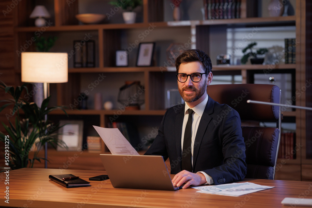Man portrait in cinematographic light. Handsome businessman is working in the office. Work behind a laptop analysis of data and graphs Man portrait in cinematographic light. Handsome businessman is working in the office. Work behind a laptop analysis of data and graphs