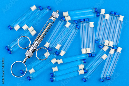 Metal syringe for local anesthesia and many carpules with anesthetic on a blue background. photo