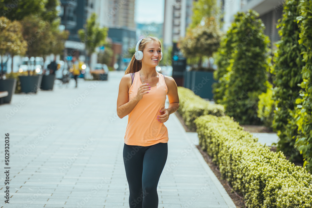 Young female runner in a sports bra is jogging in the city street. full length of Urban female runner training on summer. Sporty woman running and exercising