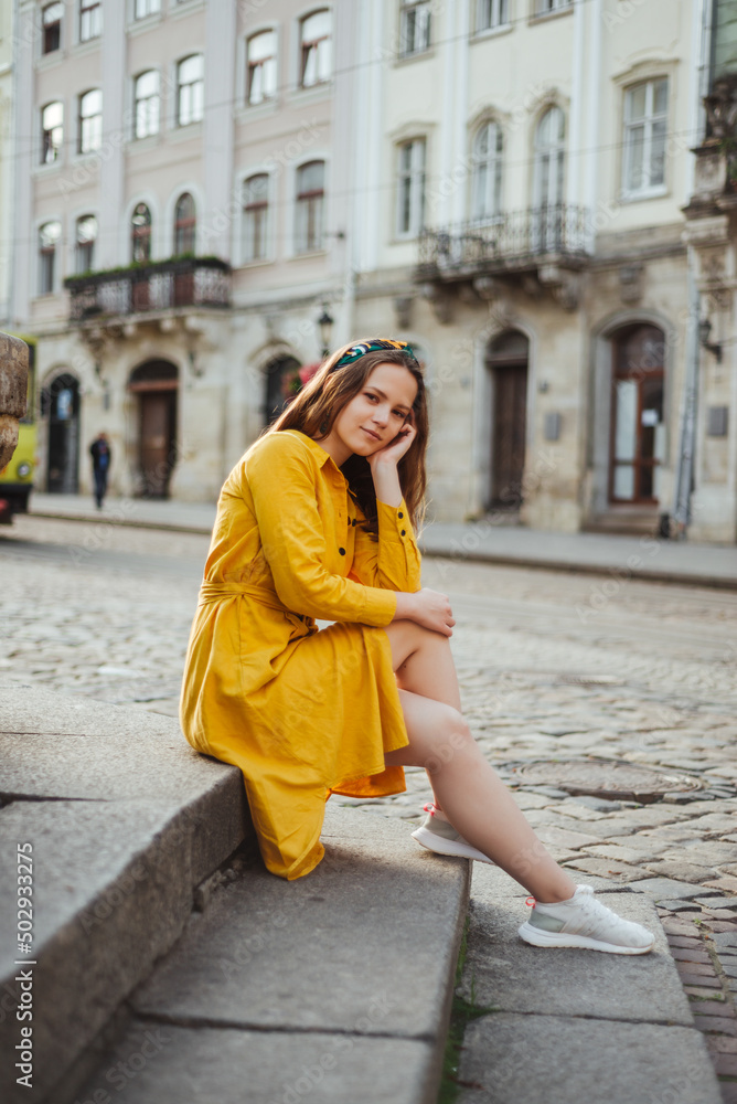 Stylish girl in yellow shirt dress sitting on old stone stairs