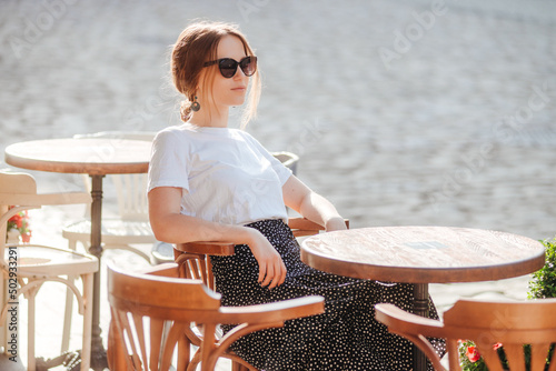 Stylish girl in sunglasses, white t-shirt and polka-dot skirt relax on the summer terrace