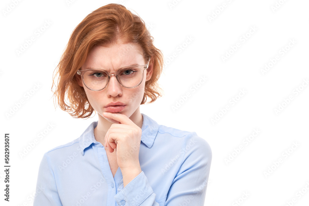 Smart redhead girl in glasses and business shirt holding chin thinks doubts, makes decision isolated on white studio background Smart redhead girl in glasses and business shirt holding chin thinks doubts, makes decision isolated on white studio background