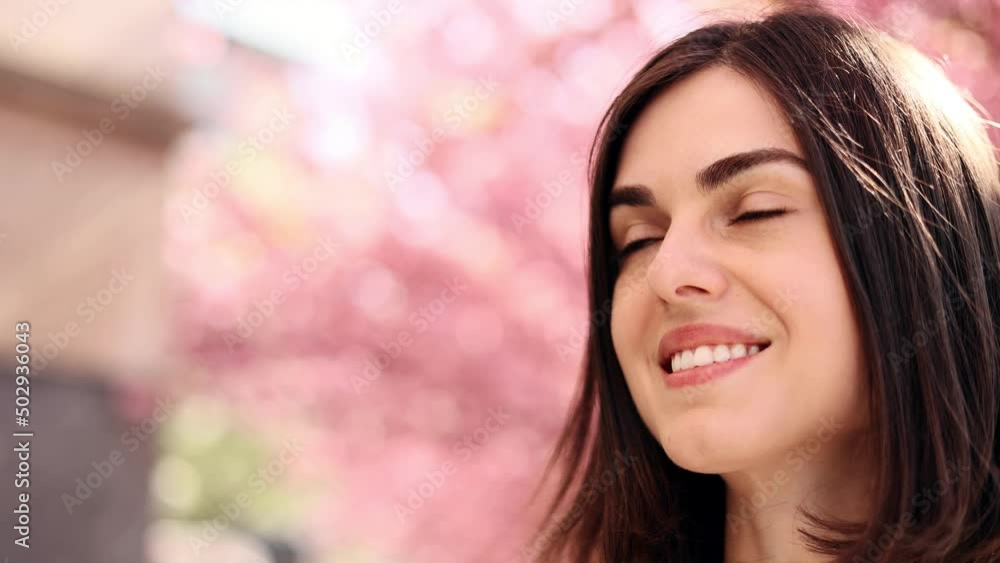 Portrait of a gorgeous dark haired woman with beautiful dark eyes standing near pink sakura trees. Attractive woman looking ahead. Copy space. Portrait of a gorgeous dark haired woman with beautiful dark eyes standing near pink sakura trees. Attractive woman looking ahead. Copy space.