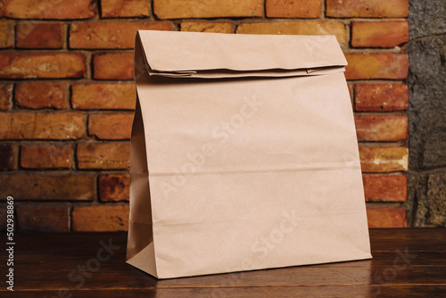 Craft paper bag on a wooden table against a brick wall. Takeaway food packaging rustic template