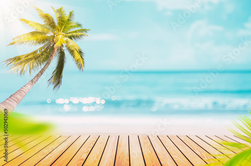 Blur tropical beach with bokeh sun light wave and palm tree on empty old wood table abstract background.