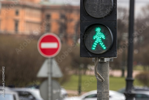 A traffic light for pedestrians with a symbol of a walking person is lit with a green light and a sign of movement is prohibited on the background.