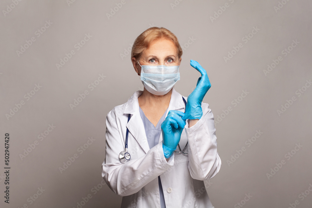 Portrait of an attractive senior female doctor in white coat and blue gloves Portrait of an attractive senior female doctor in white coat and blue gloves