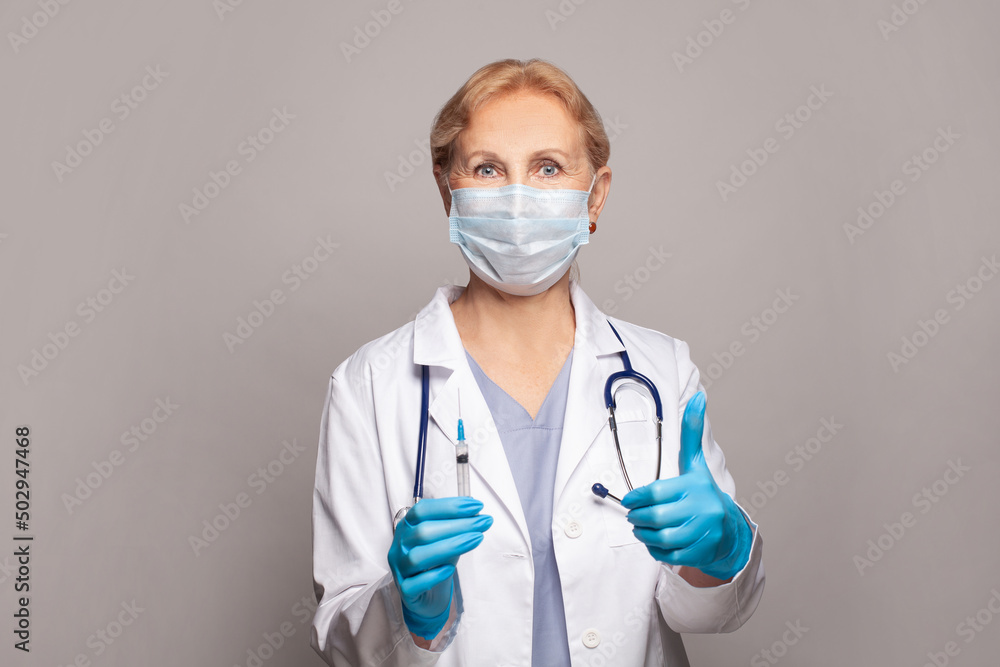 Mature female nurse or doctor holding syringe and showing thumb up