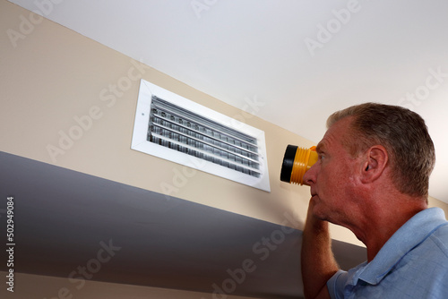 Man Inspecting a Home Rectangle Wall Air Vent with a Flashlight