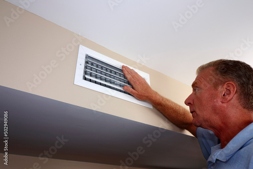 White Male Hand on a White Air Duct Vent Grille on a Beige Wall
