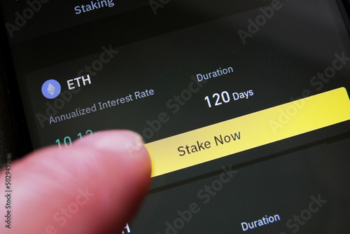 Slika na platnu A cryptocurrency investor about to stake Ethereum on a crypto exchange mobile phone app to earn high interest rate