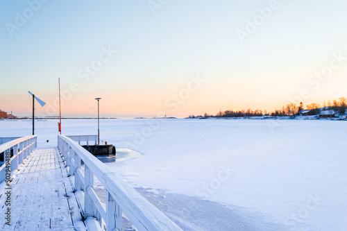 Frozen water of the seaside in Helsinki in winter, a wooden pier covered in white snow  © eugpng