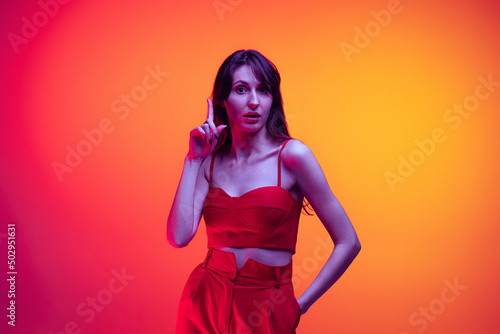 Have ideas. Studio shot of young girl, student with long hair isolated over orange studio background in neon light. Concept of emotions, art, beauty