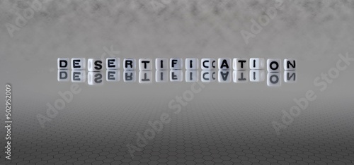 desertification word or concept represented by black and white letter cubes on a grey horizon background stretching to infinity