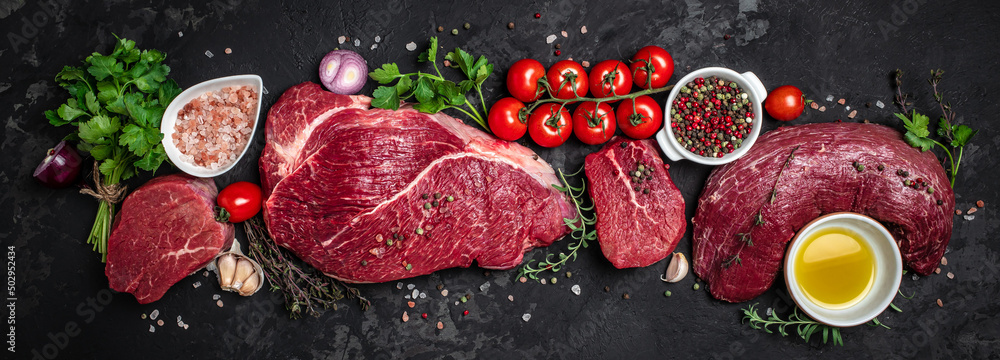 Set of fresh raw beef steak with spices ready to cook on a dark background. Long banner format. top view Set of fresh raw beef steak with spices ready to cook on a dark background. Long banner format. top view