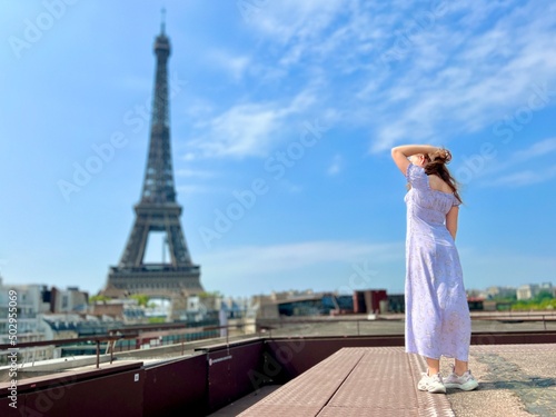 a beautiful teenage girl looks into the frame leaning against the backdrop of the Eiffel Tower She smiles and seems to be showing come here great advertisement for a trip to Paris. High quality photo