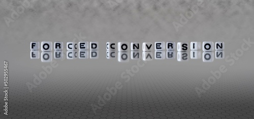 forced conversion word or concept represented by black and white letter cubes on a grey horizon background stretching to infinity