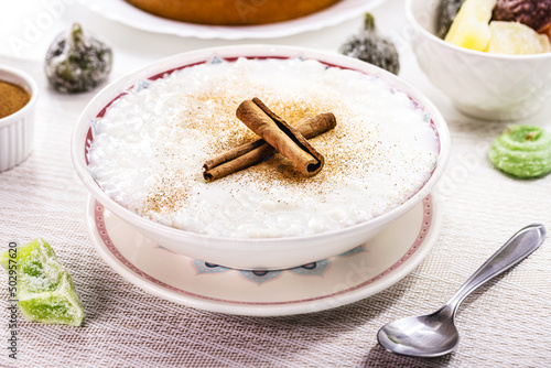 rice pudding bowl, homemade pudding made from ground rice, sweetened with cinnamon powder and cinnamon bark. Rural Brazilian sweets in the background, typical June festival food