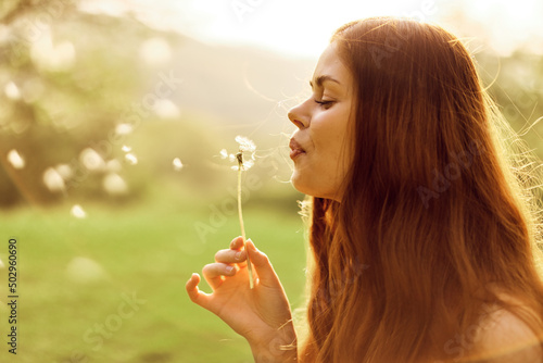 A young woman holds a dandelion in her hands and blows on it  the seeds of the dandelion fly through the air to grow new flowers. Caring for the Earth s Ecology