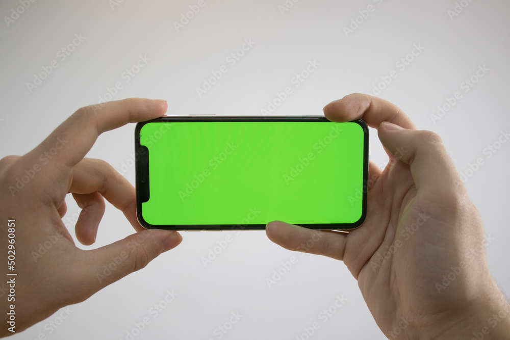 Holding an iPhone in hand. Green Screen on the phone. Mock-up of an iPhone. Apple product in hand. Vertical tilt of the phone. Holding an iPhone in hand. Green Screen on the phone. Mock-up of an iPhone. Apple product in hand. Vertical tilt of the phone.