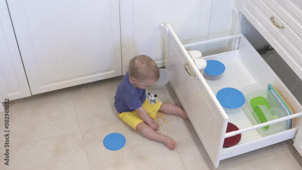 Toddler playing at home, one year old baby boy opening the drawer in the kitchen, curious child taking out kitchen utensils. Infant learn exploring environment. High quality 4k footage Toddler playing at home, one year old baby boy opening the drawer in the kitchen, curious child taking out kitchen utensils. Infant learn exploring environment. High quality 4k footage