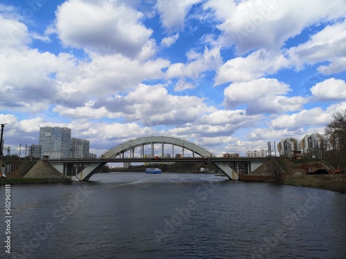 Bridge over the river Moscow against the background of a blue sky with clouds. A motor ship in the distance © Ann
