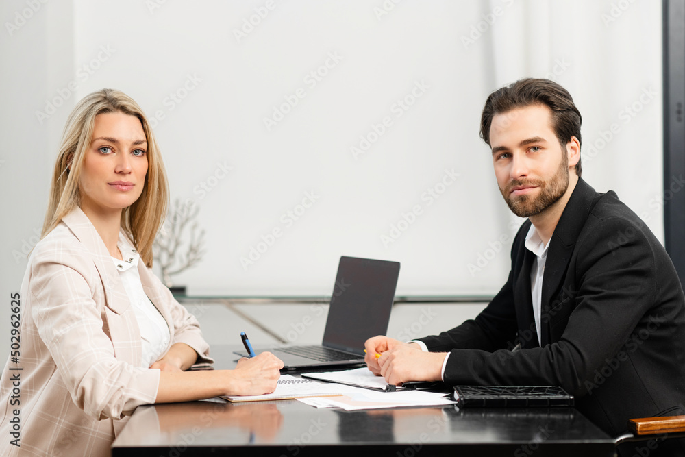 Young caucasian coworkers working out business strategy together and discuss tasks while sitting at the office desk and looking at the camera. Team work Young caucasian coworkers working out business strategy together and discuss tasks while sitting at the office desk and looking at the camera. Team work