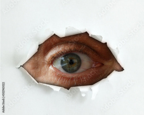 Spy eye peeking through a hole in the paper. Eye looking through a hole in a white empty paper poster